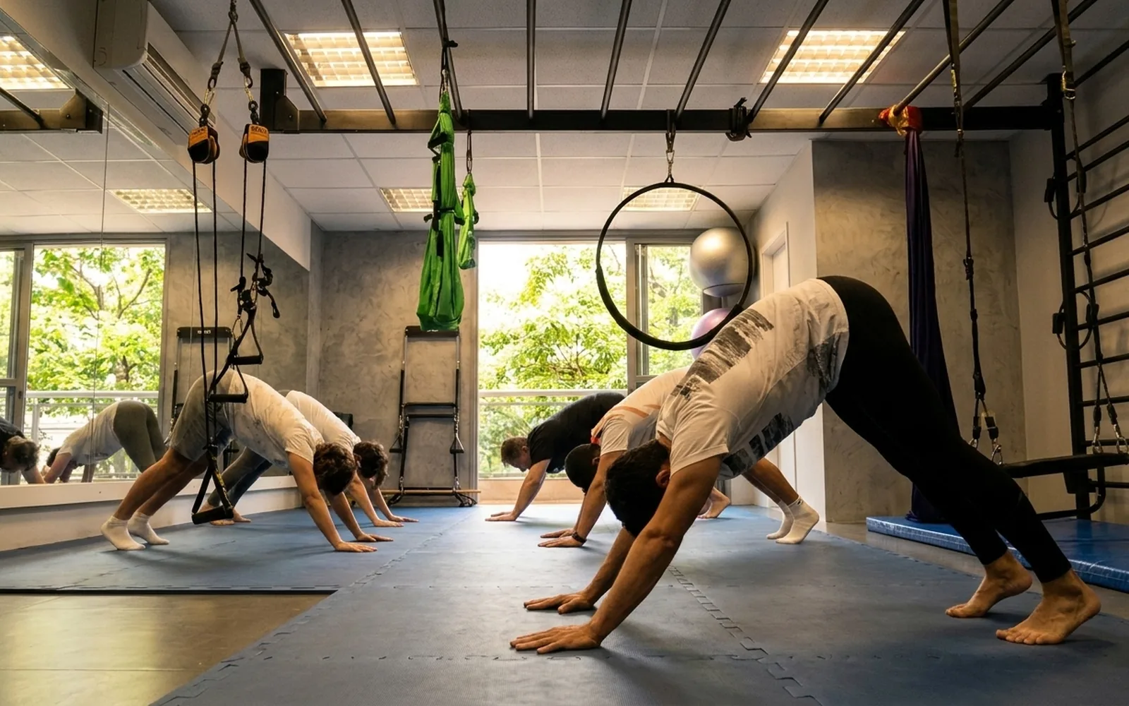 Turma em exercício de alongamento sobre os tatames do estúdio da Saúde Urbana, com janelas para as árvores